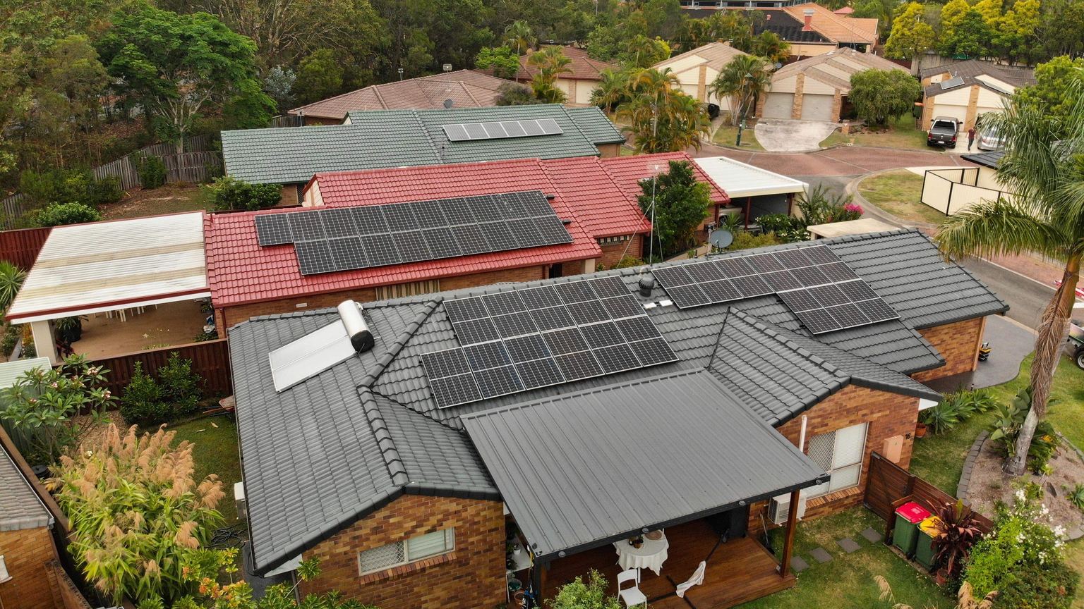 Aerial view of brick homes on a suburban street with solar panels on their tiled roofs